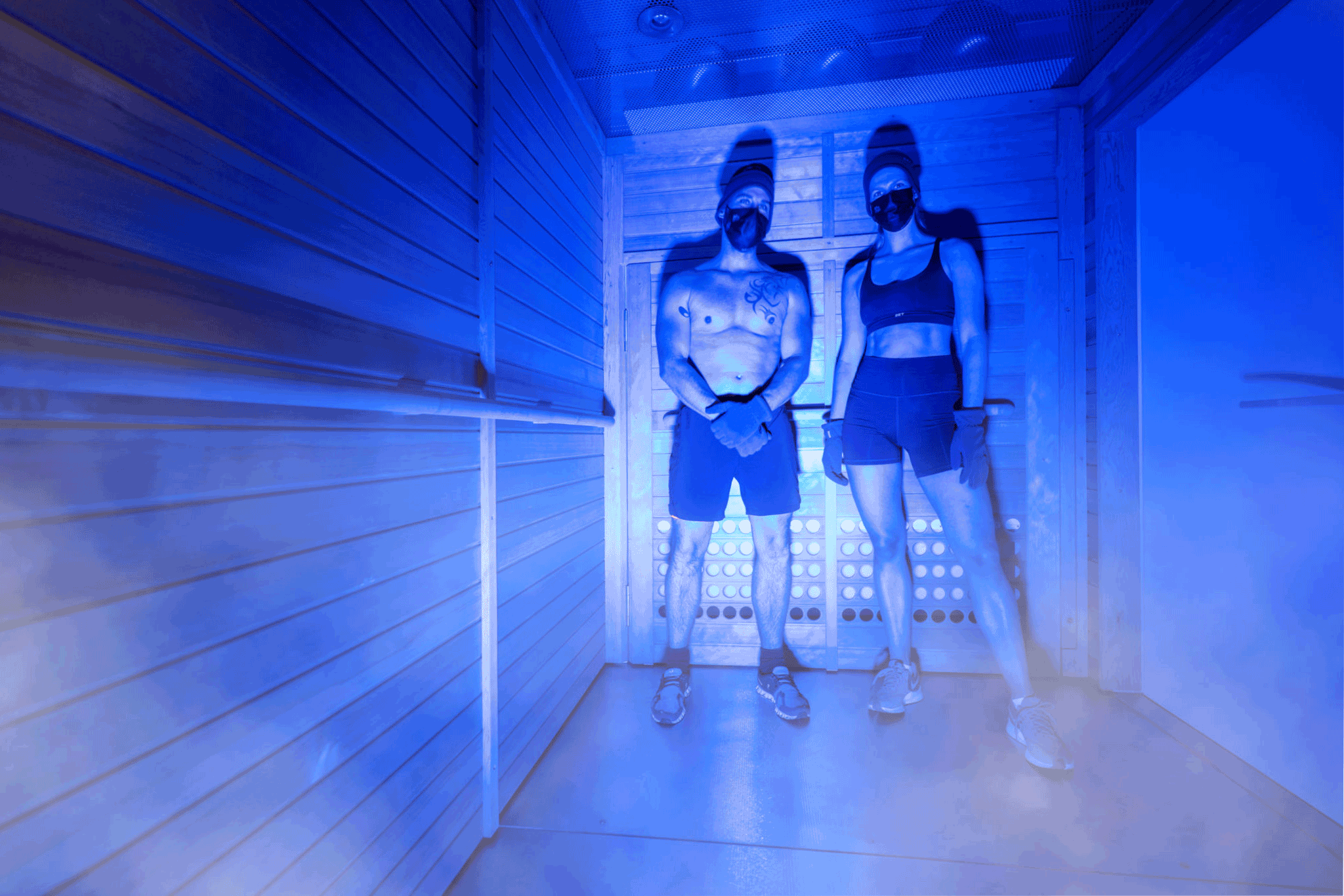 Two people standing together in a blue-lit cryotherapy chamber